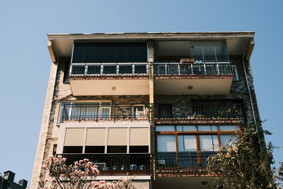 A modern apartment building facade with blooming flowers in the foreground under a clear blue sky.